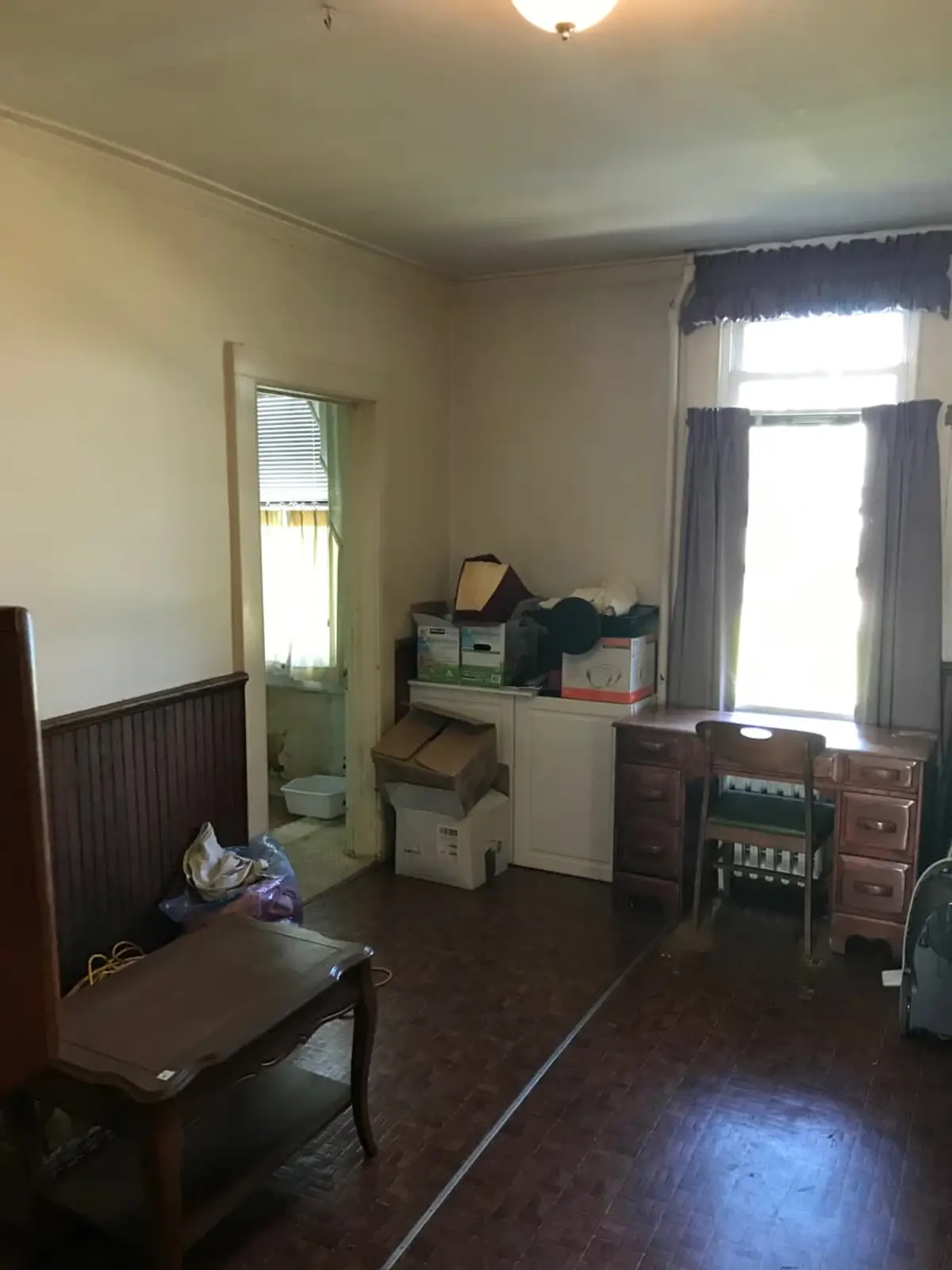 Selling a house with tenants in it in Lindenhurst: dated room with wainscoting, a desk and stacked boxes