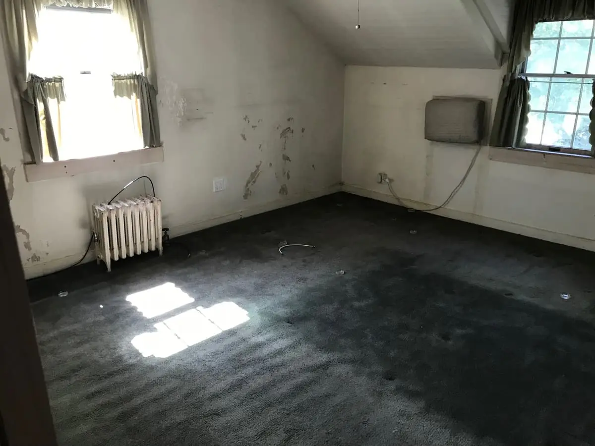 Selling a house after a life change in Lindenhurst: empty attic bedroom with dark carpet and an old radiator