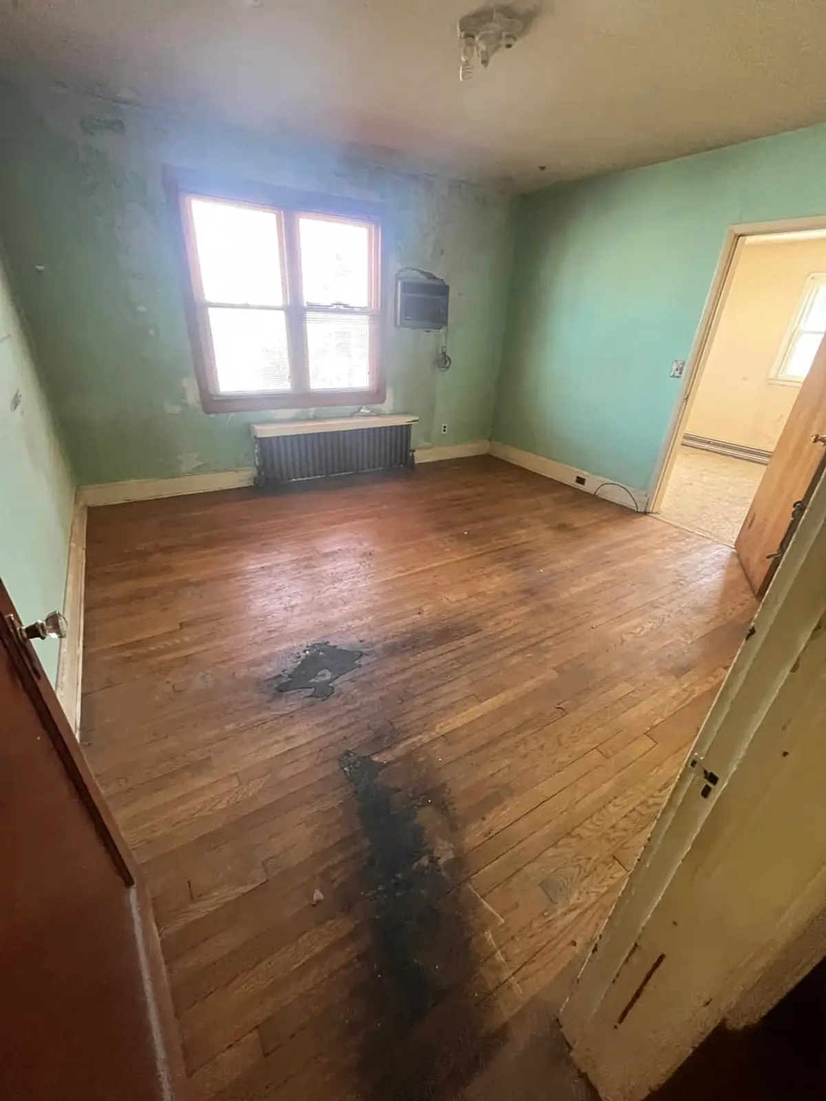 Selling a house with foundation problems in Lindenhurst: empty green bedroom with a dark stain across the wood floor
