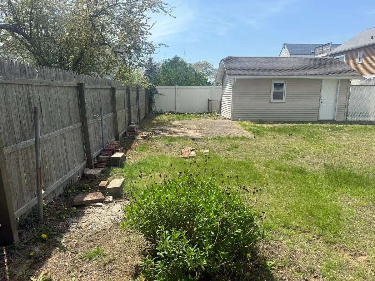 Selling a house with a failed cesspool in Lindenhurst: fenced backyard with patchy grass leading to the garage